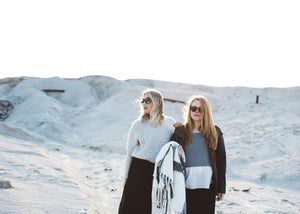 Two women walking along a snowy hill wearing Nöz's colorful and cool nözscreen. 